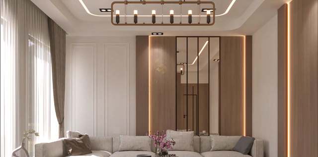 Living-room feature wall with a walnut-slatted panel framed by warm LED reveals, a black-framed mirror inset, white wainscot panels, a stepped cove-lit ceiling and a bronze six-light linear chandelier above a linen sofa, sheer curtains glowing with daylight.